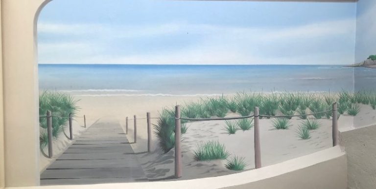 Trompe l'oeil peint sur mur d'une Plage tranquille avec une passerelle et des dunes de sable sous un ciel nuageux.