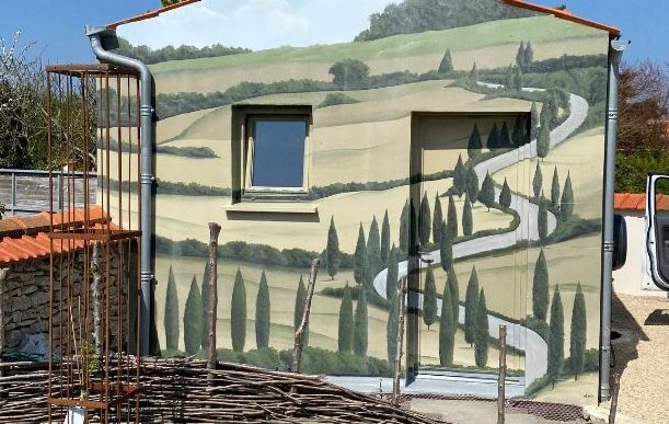 Mur de bâtiment décoré d'une fresque représentant un paysage vallonné avec des arbres et une route.