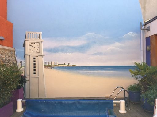Fresque murale représentant une plage avec une horloge et un ciel bleu.
