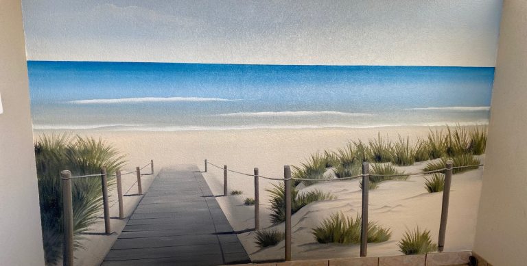 Peinture trompe oeil chemin en bois menant à une plage de sable avec mer bleue à l'horizon.